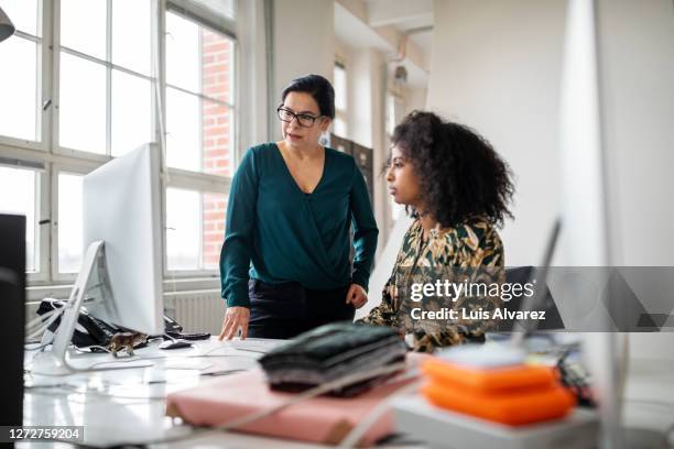 senior businesswoman helping young colleague in office - co workers looking at computer stock-fotos und bilder