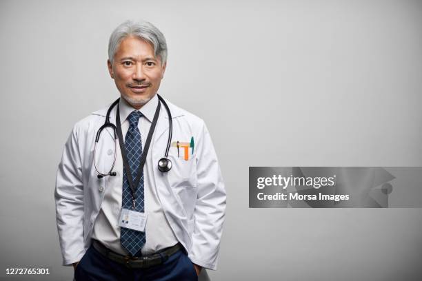 japanese mature doctor in lab coat against white background - doctor lab coat stock-fotos und bilder