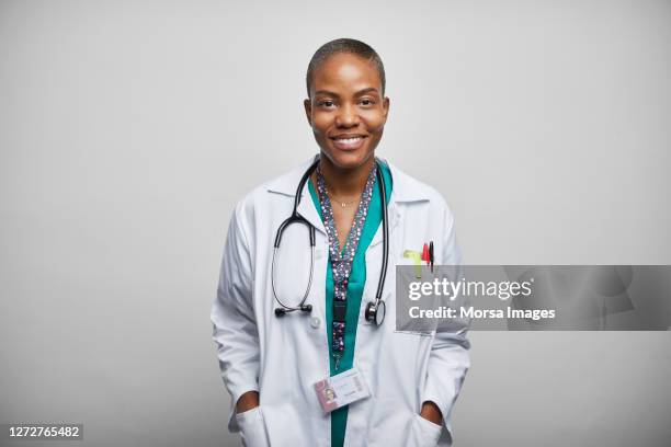 female doctor with hands in pockets over white background - blouse blanche femme photos et images de collection