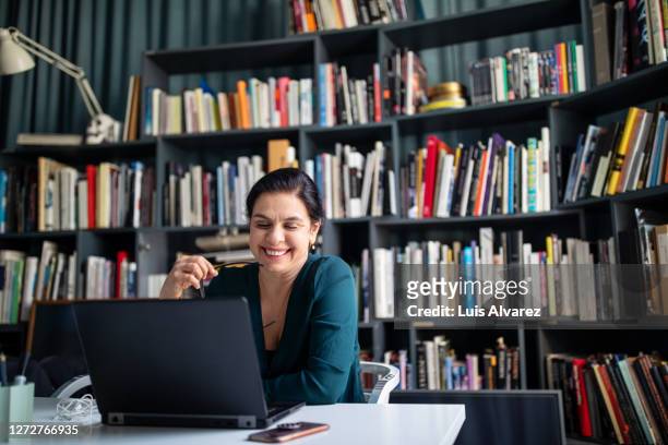 businesswoman looking at her laptop and smiling - woman business desk front laptop office fotografías e imágenes de stock