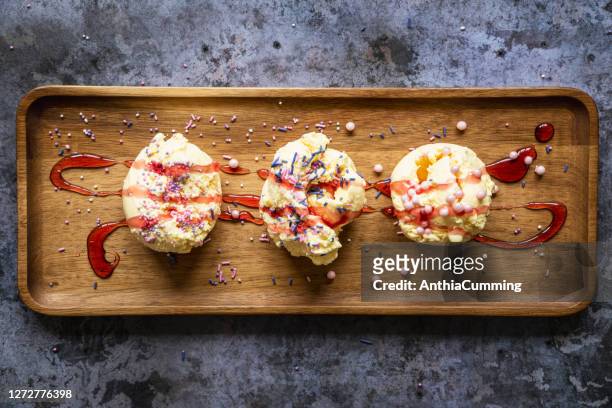 three scoops of vanilla ice cream covered in sprinkles and sauce - strawberry syrup stock pictures, royalty-free photos & images