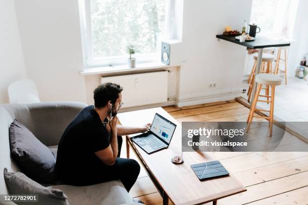 man works with laptop in his living room - wide shot of people stock pictures, royalty-free photos & images