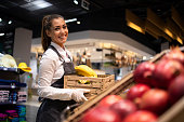 Working in grocery store. Supermarket worker supplying fruit department with food. Female worker holding crate with fruits.