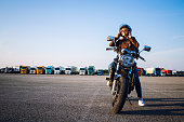 Beautiful sexy brunette woman in leather jacket sitting on retro style motorcycle getting ready for the ride. Riding motorbike. Copy space for text provided.
