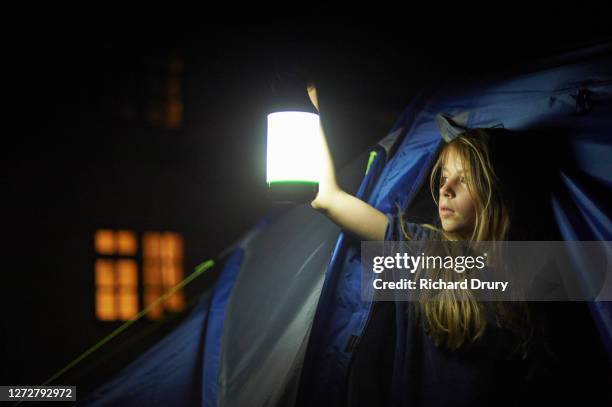 a young girl holding a lantern and looking out of her tent - zelt nacht stock-fotos und bilder