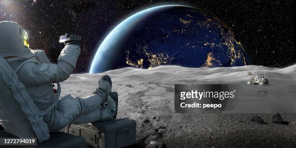 astronaut sitting on moon recording sunrise on earth with smartphone - copy space stock pictures, royalty-free photos & images