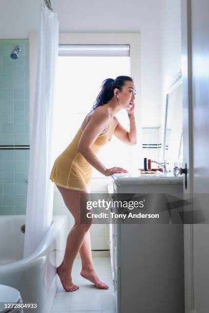 young woman looking into bathroom mirror - woman-looking-into-mirror-full-body stock pictures, royalty-free photos & images