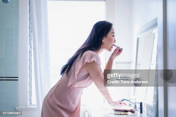 young woman applying lipstick in bathroom - brightly lit bathroom stock pictures, royalty-free photos & images