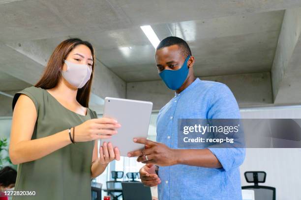 businesswoman and businessman having discussion about business while using digital tablet in office while wearing protective face masks - cloth face mask stock pictures, royalty-free photos & images