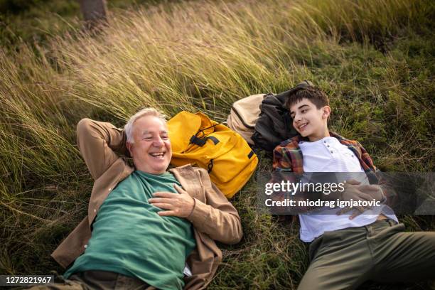 großvater und enkel liegen auf gras und genießen gemeinsam zeit beim wandern - teenager alter stock-fotos und bilder