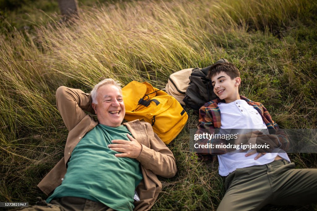 Grand-père et petit-fils se trouvant sur l’herbe et appréciant le temps ensemble pendant la randonnée