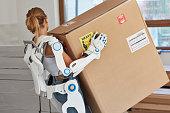 Professional female home mover in powered exoskeleton. Carrying heavy box