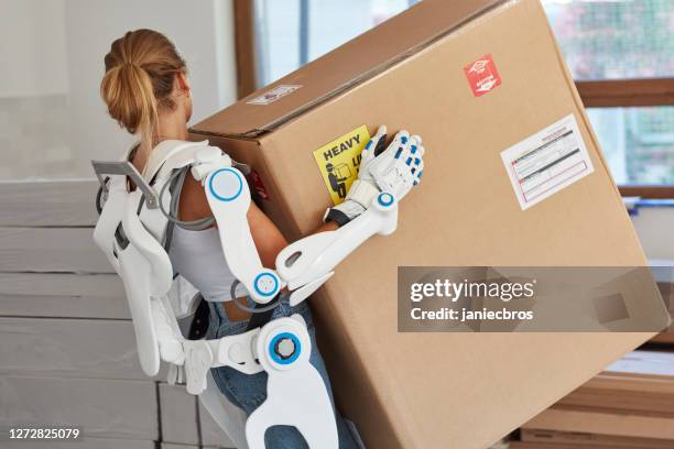 professional female home mover in powered exoskeleton. carrying heavy box - powered exoskeleton stock pictures, royalty-free photos & images