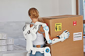 Professional female home mover in powered exoskeleton. Carrying heavy box