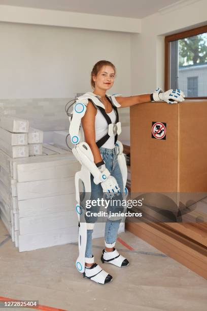 professional female home mover in powered exoskeleton. carrying heavy box - exoskeleton stock pictures, royalty-free photos & images