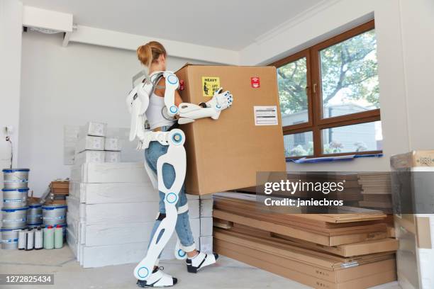 professional female home mover in powered exoskeleton. carrying heavy box - exoskeleton stock pictures, royalty-free photos & images