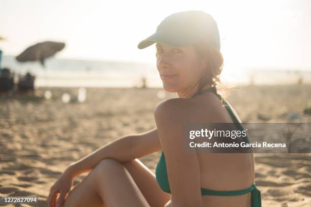 thirty years old woman with cap and bikini at sunset looking at camera for portrait - woman 30 years old portrait stock pictures, royalty-free photos & images