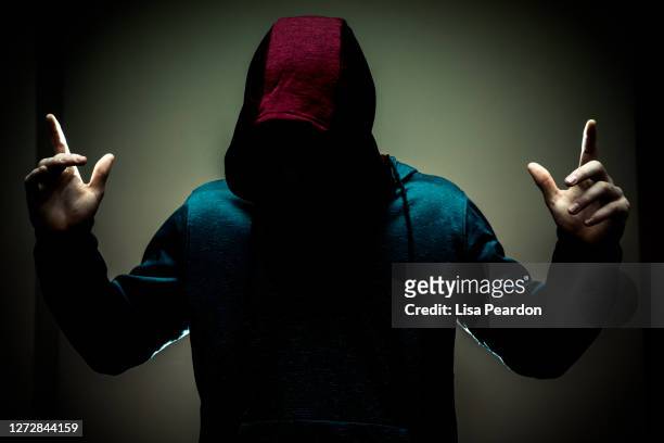 studio portrait of young adult male with mint green background head down in and shadowed by red hoodie.. - rapper isolated stock pictures, royalty-free photos & images