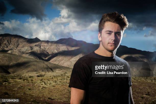 handsome young male adult looking into the camera lit by dramatic lighting with mountains and dramatic sky behind him. - confidence male landscape stock-fotos und bilder