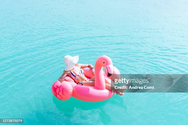 woman on pink flamingo floating on sea - flamingos stock-fotos und bilder