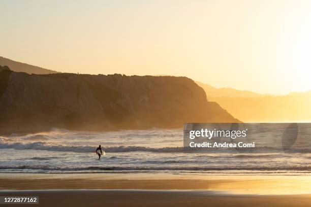 surfer with surfboard on beach during sunset. spain - comunidad autonoma del pais vasco stock-fotos und bilder