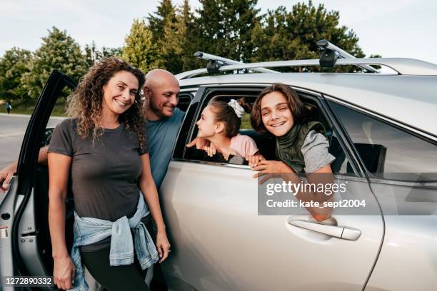 familia caucásica cerca del coche mirando a la cámara. dos niños y padres sonriendo. - four people in car fotografías e imágenes de stock