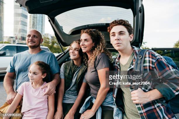 caucasian family looking straight and sitting in the trunk. three kids and parents smiling. - three children stock pictures, royalty-free photos & images