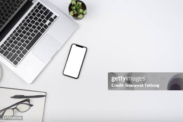 modern white office desk table with laptop computer, smartphone with black screen over a notebook and cup of coffee. top view. - flatlay stock-fotos und bilder