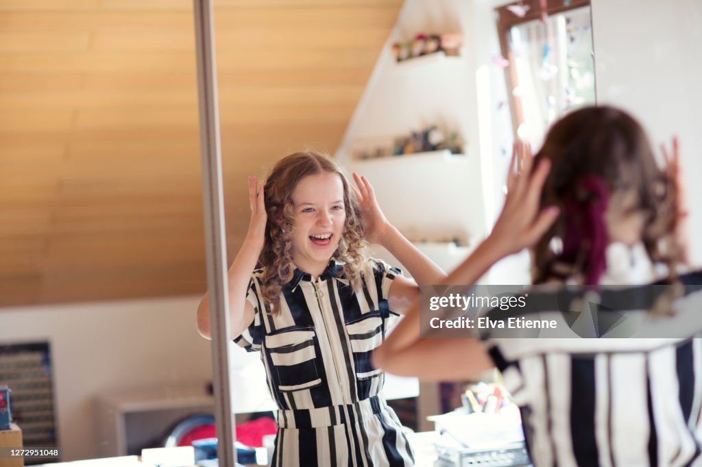 Laughing teenage girl seeing how curly her hair is in a mirror after using socks as curlers
