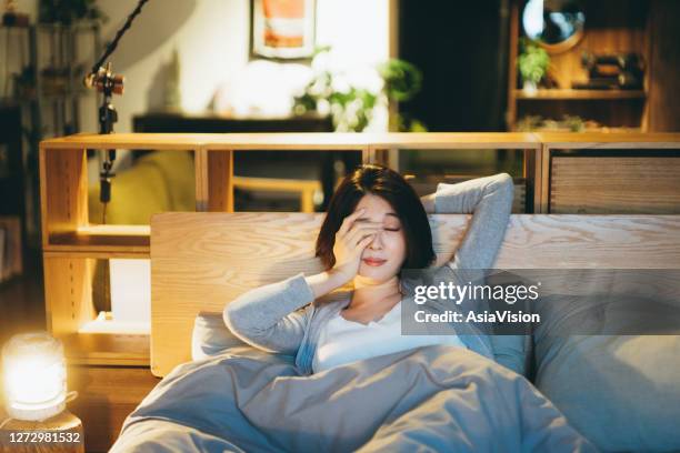 young asian woman lying on the bed in the bedroom, feeling tired and sleepy, rubbing her eyes and ready to sleep in the evening - rubbing eyes stock pictures, royalty-free photos & images