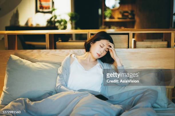 若いアジアの女性は病気で頭痛に苦しんで、ベッドに横たわって家で休む - 欲求不満 ストックフォトと画像