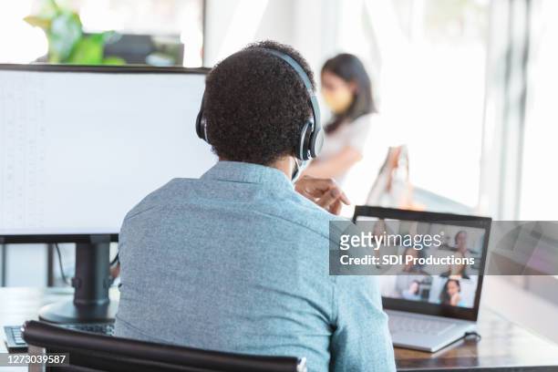 man uses bluetooth headphones to video conference with colleagues - bluetooth stock pictures, royalty-free photos & images