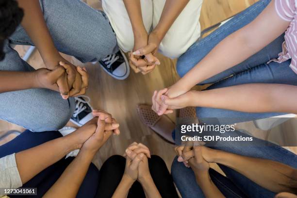 vista ad angolo alto mani giunte di gruppo seduto in cerchio - bambini seduti in cerchio foto e immagini stock