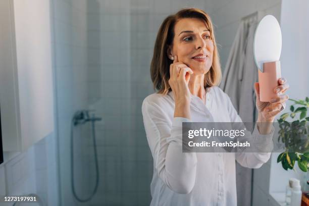 anti age rituals: een gelukkige volwassen vrouw die zich in de spiegel in de badkamer bekijkt - women wrinkle stockfoto's en -beelden