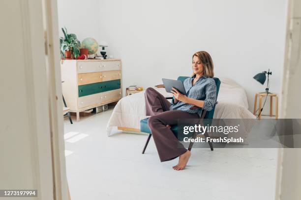 working from home: beautiful senior woman using a digital tablet at home - armchair imagens e fotografias de stock