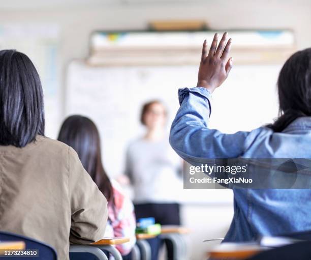 female teenage student raising hand in classroom - teacher taking attendance stock pictures, royalty-free photos & images