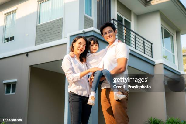 asian family with father and mother standing and carry daughter in front of thier house look happy and smile. happiness and harmony in family life. - family smile photos et images de collection