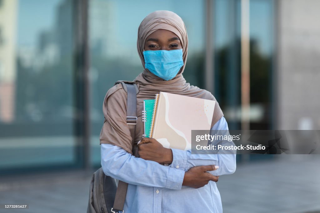 Education During Pandemic. Black muslim female student in mask with workbooks outdoors