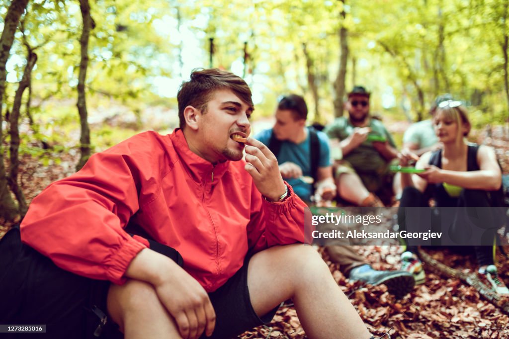 Young Male Chewing Bread Piece During Hiking Breakfast With Friends