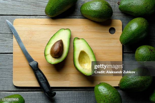 avocado cut in half on a chopping board. next to the whole fruit and a knife. - avocado stock-fotos und bilder