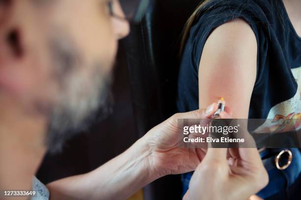 over the shoulder view of doctor giving hpv vaccination to teenager in a home environment - injecteren stockfoto's en -beelden