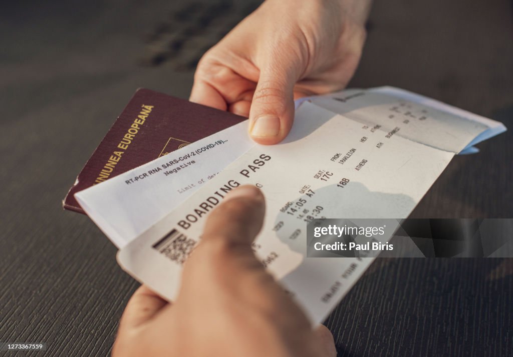 Hand of passenger with a RT-PCR RNA Covid test with passport and a plane ticket at the airport check-in attendant