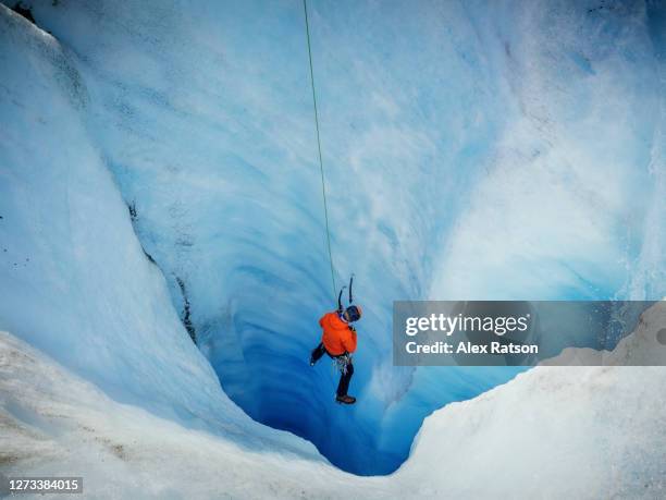 man in red jacket ice climbing turquoise coloured ice on the athabasca glacier - crevasse stock pictures, royalty-free photos & images