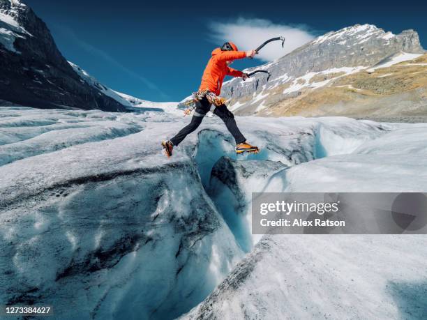 ice climber takes running jump across a large crevasse on glacier - ice climbing stockfoto's en -beelden