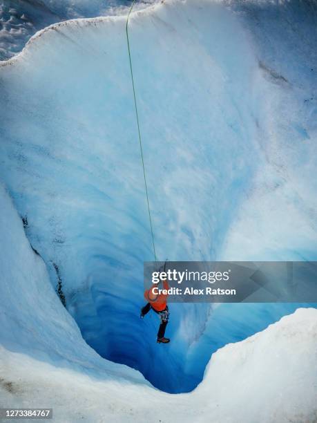 man in red jacket ice climbing turquoise coloured ice on the athabasca glacier - jasper canada stock pictures, royalty-free photos & images