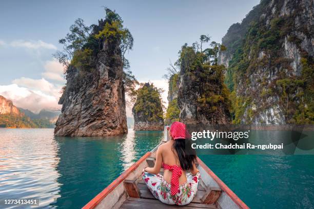 asia travel thailand. tourists in red bikini sets are holding hands with fun on the boat at khao sok national park, chiewlarn dam, thailand. chiao lan khao sok dam is a tourist attraction in surat thani province of thailand.happy woman traveler on boat he - phuket - fotografias e filmes do acervo