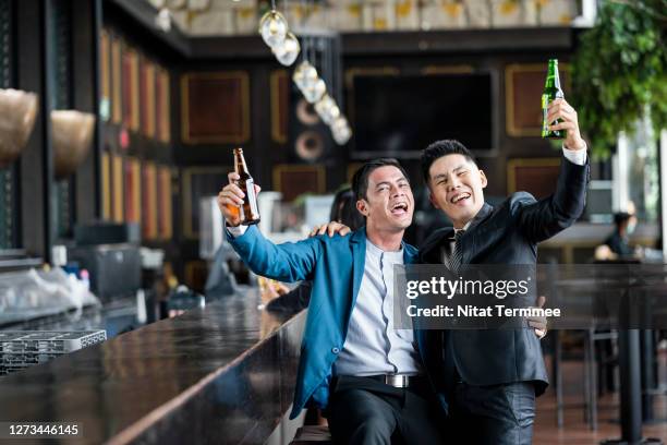 two businessman having fun while drinking a beer having a laugh at bar counter. relax after hardworking day. - pub mates stock-fotos und bilder