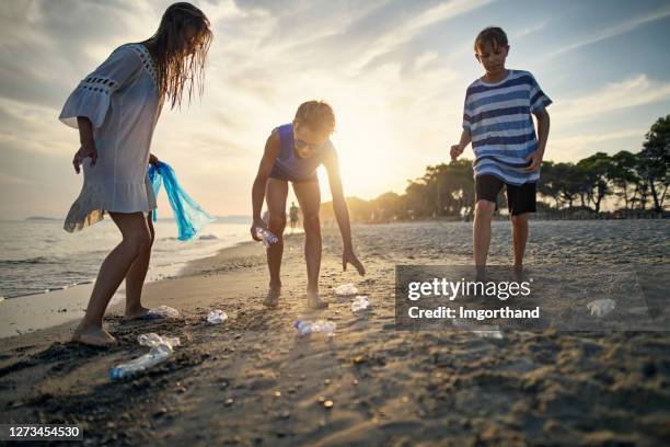 three kids cleaning up the beach - picking up garbage stock pictures, royalty-free photos & images