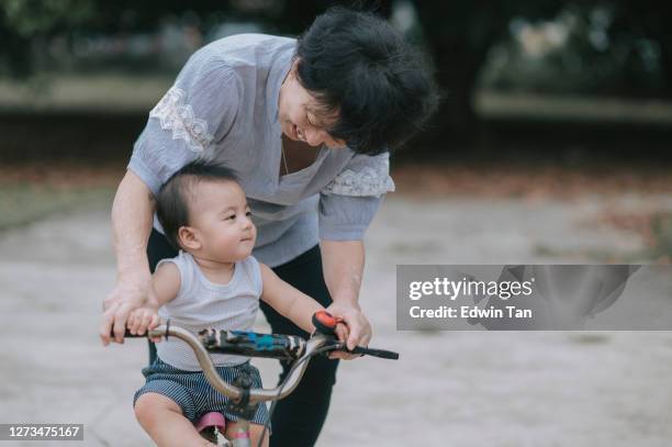 aziatische chinese actieve hogere vrouw die haar kleinzoonbabyjongen leert hoe te om een fiets in openbare de ochtend van het parkweekend te berijden - bukken stockfoto's en -beelden