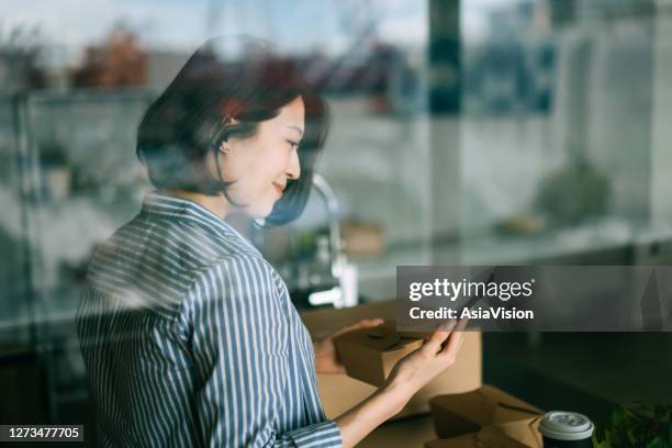 mooie glimlachende jonge aziatische vrouw die zich door het keukenbalie bevindt, dat voedsel met behulp van mobiel appapparaat op smartphone voor een de dienst van de voedselbezorging opdracht eert. technologie maakt het leven zoveel gemakkelijker - customer journey stockfoto's en -beelden